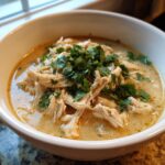 A close-up of a creamy bowl of keto white chicken chili, topped generously with fresh chopped cilantro or parsley.