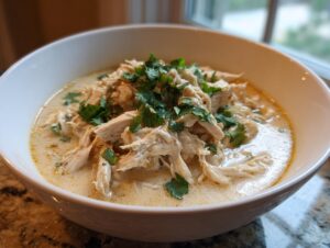A close-up of a white bowl filled with creamy keto white chicken chili topped with fresh cilantro.
