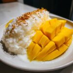 Close-up of vibrant mango sticky rice, featuring sweet sticky rice topped with toasted sesame seeds next to sliced fresh mango.