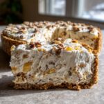 A thick slice of creamy Million Dollar Pie with a graham cracker crust, topped with pecans.