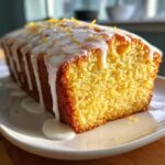 A close-up of a freshly baked lemon loaf cake topped with thick white glaze and lemon zest.
