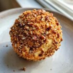 Close-up of a perfectly formed cheese ball recipe coated entirely in chopped pecans and brown crumbs.