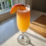 A fizzy, orange-hued bellini recipe cocktail garnished with a fresh peach slice in a champagne flute.