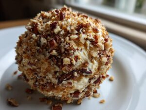 A close-up, featured image of a creamy cheese ball recipe coated entirely in chopped pecans, sitting on a white plate.