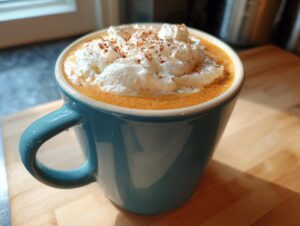 Close-up of a homemade pumpkin spice latte topped with whipped cream and cinnamon in a blue mug.