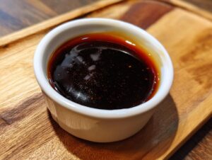 Close-up of thick, dark homemade teriyaki sauce in a small white ramekin on a wooden surface.
