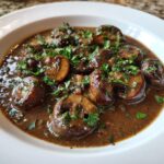 A close-up of a rich mushroom sauce filled with whole, browned mushrooms and topped with fresh parsley.