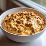 A close-up of a warm, cheesy sausage cream cheese dip topped with browned sausage crumbles in a white serving bowl.