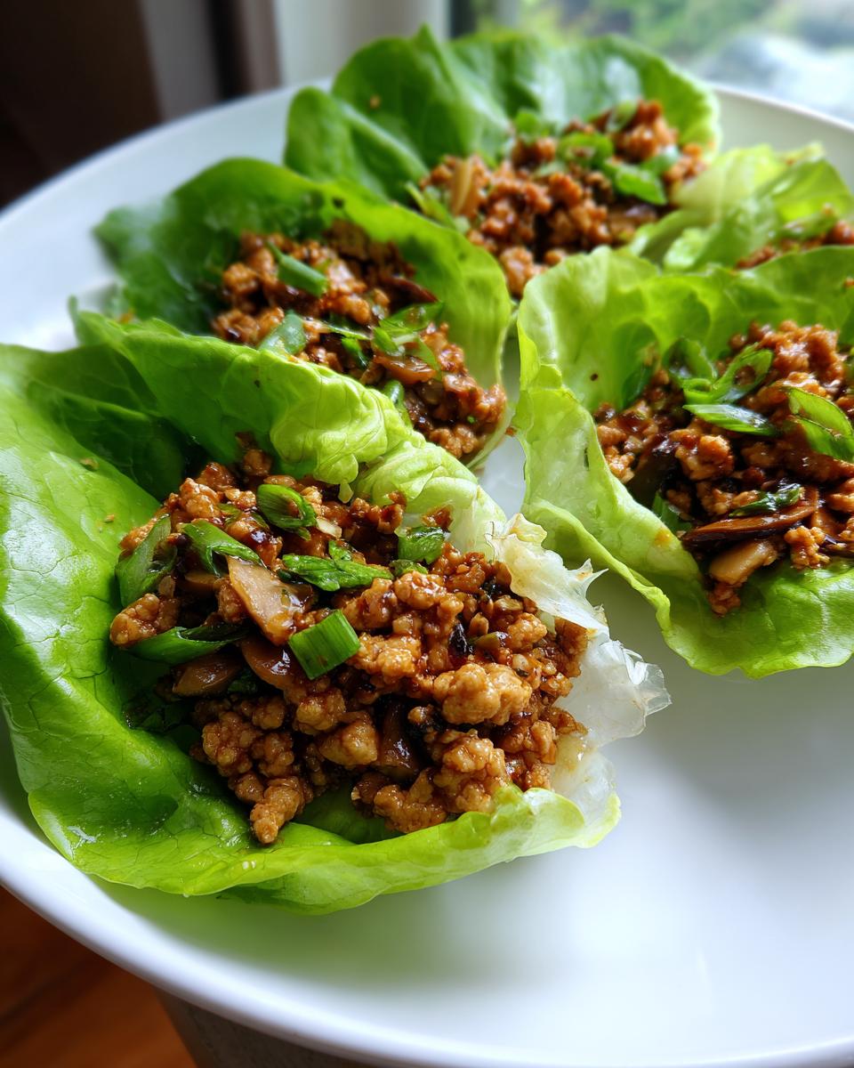 Four servings of delicious chicken lettuce wraps filled with seasoned ground chicken and topped with green onions, ready to eat.
