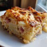 A close-up of a hearty slice of scalloped potatoes and ham casserole with a bubbly, browned cheese crust.