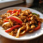 Close-up of seasoned chicken strips mixed with sautéed red peppers and onions, ready for crockpot chicken fajitas.