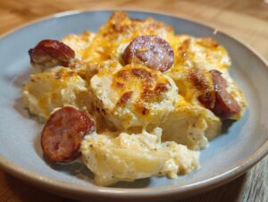 A close-up of a serving of creamy pierogi casserole topped with melted cheese and slices of browned sausage.