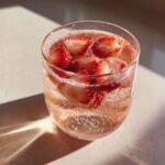 Close-up of a glass filled with bubbly pink champagne punch garnished with fresh strawberry slices.
