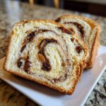 Two thick slices of homemade raisin bread showing a beautiful cinnamon swirl and plump raisins.