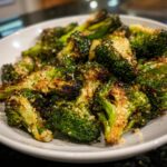 Close-up of crispy, charred smashed broccoli florets topped with grated Parmesan cheese in a white bowl.