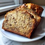 Close-up of three moist slices of sourdough banana bread with visible nuts and chocolate chips on a white plate.