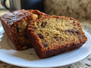 Close-up of two thick slices of moist sourdough banana bread featuring a dark, caramelized crust and visible chocolate chips.