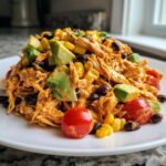 A mound of creamy southwest chicken salad topped with chunks of avocado, black beans, corn, and cherry tomatoes.