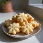 A pile of golden, star-shaped butter cookie treats dusted lightly with sugar on a small plate.