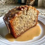 A moist slice of sweet alabama pecan bread topped with a pecan glaze, sitting on a white plate.