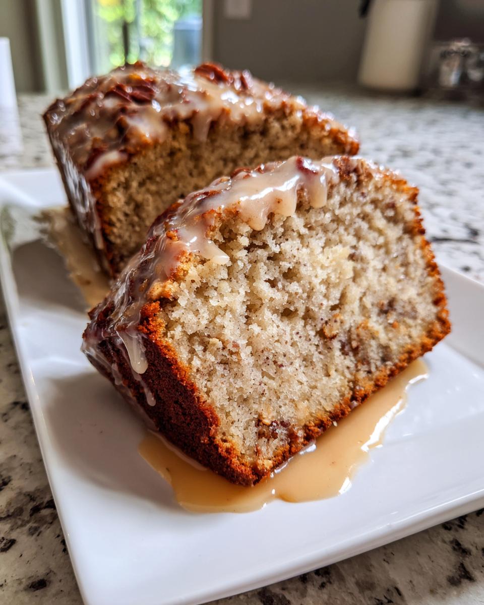 A close-up of two slices of sweet Alabama pecan bread topped with a thick, dripping caramel glaze on a white plate.
