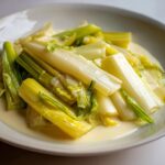 Close-up of perfectly cooked braised leeks served in a light, creamy sauce on a white plate.