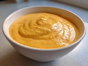 Close-up of rich, orange-yellow beer cheese dip swirled in a white bowl, ready for dipping.