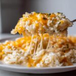 A spoonful of creamy, cheesy rice is lifted, showing long, stretchy strings of melted cheese from the cheesy rice dish.
