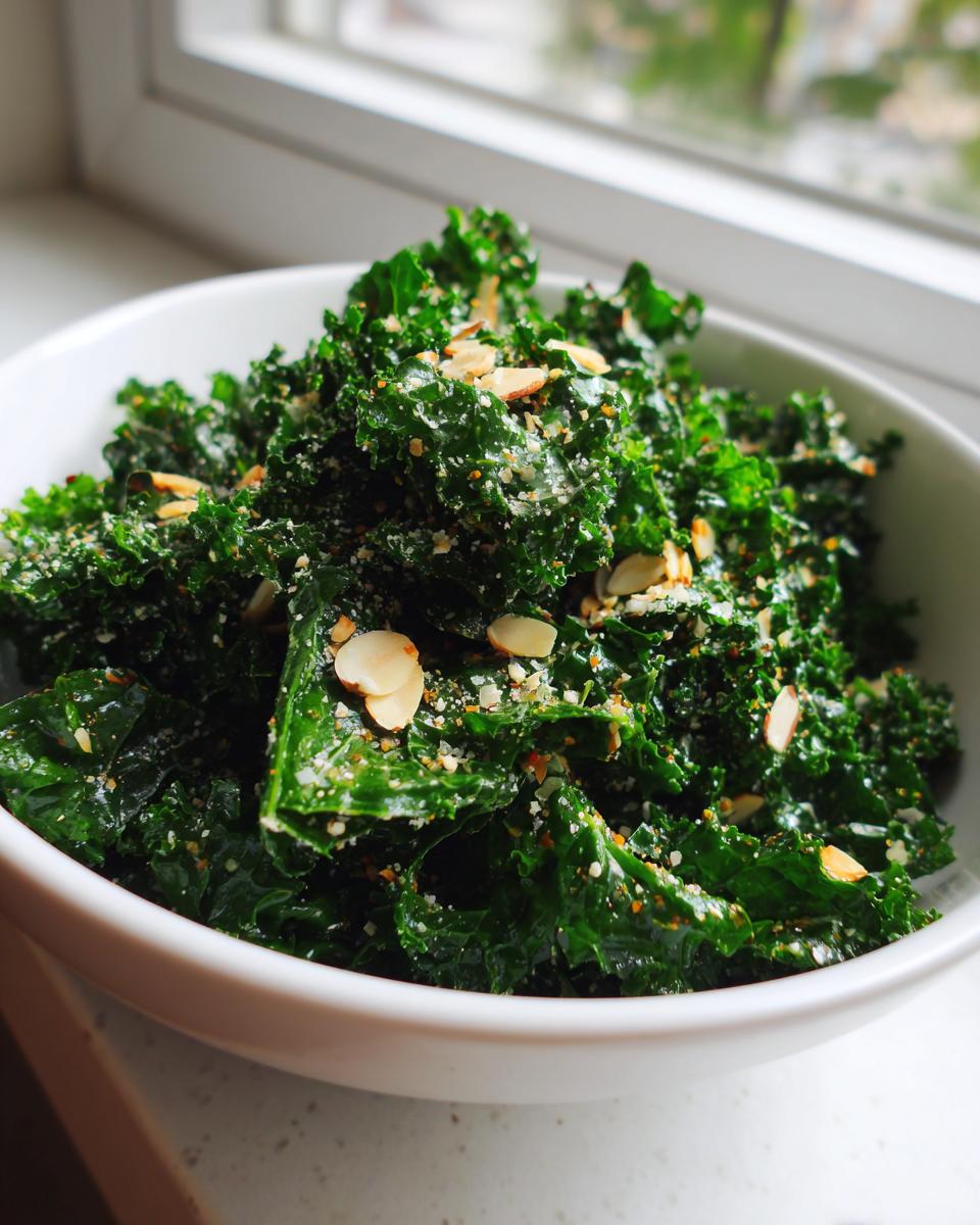 A close-up of a vibrant kale salad topped with sliced almonds and grated cheese, served in a white bowl.