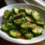 Close-up of vibrant green slices of asian cucumber salad tossed in a savory dressing with sesame seeds.