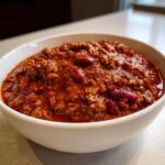 Close-up of a hearty bowl of rich, dark red chili loaded with ground meat and kidney beans.