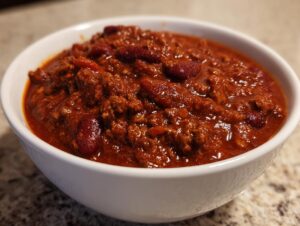 Close-up of a white bowl filled with rich, thick, award winning chili featuring ground meat and kidney beans.