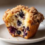 A moist blueberry muffin with a bite taken out, showing juicy blueberries and a crunchy streusel topping.