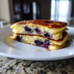 Close-up of two thick slices of blueberry sheet pan pancakes stacked on a white plate, showing fluffy interior.