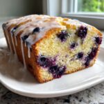 Close-up of a moist blueberry zucchini bread loaf drizzled with white glaze, showing vibrant blueberries inside.
