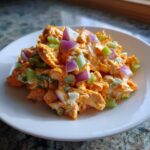 A close-up of a scoop of bright orange buffalo chicken salad topped with diced red onion and celery.