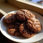 A stack of rich, dark molasses cookies covered in sparkling granulated sugar resting on a white plate.