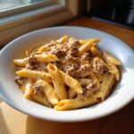 A close-up shot of creamy beef pasta featuring penne noodles coated in a rich, cheesy sauce with ground beef.