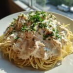 A plate of spaghetti topped with creamy crock pot angel chicken and fresh parsley.