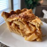 Close-up of a thick slice of homemade apple pie showing flaky crust and caramelized apple filling.