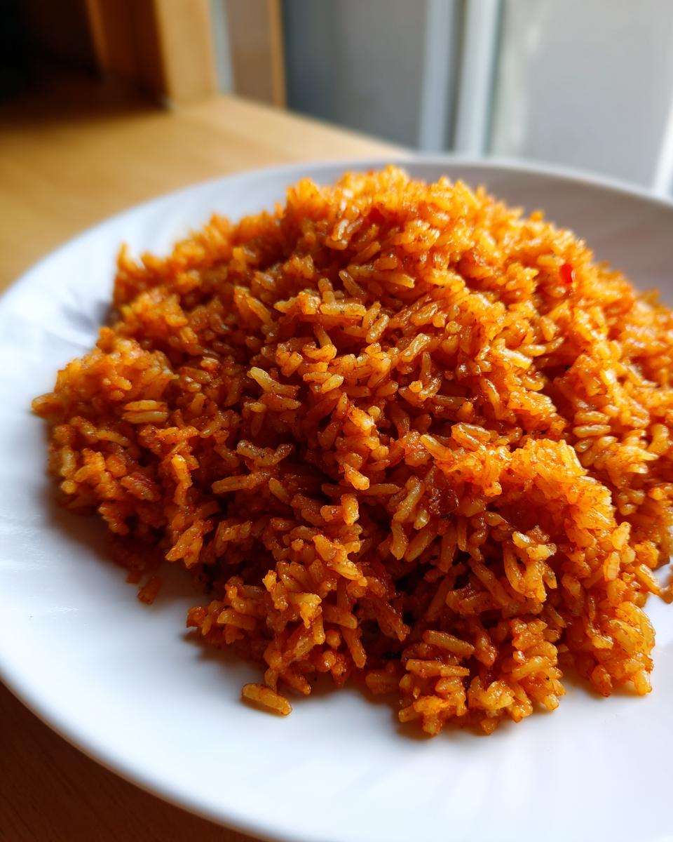 A close-up shot of a mound of perfectly cooked, vibrant orange jollof rice served on a white plate.