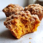 Close-up of a fluffy sweet potato muffins, bitten open to show the moist orange interior and cinnamon sugar topping.