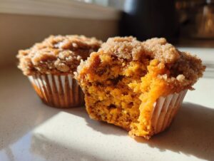 Close-up of a fluffy sweet potato muffin cut in half, showing its moist orange interior and cinnamon streusel topping.