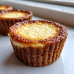 Close-up of a perfectly baked cheesecake cupcake with a golden brown crust and creamy center.