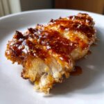 Close-up of a piece of crispy hot honey chicken, showing the flaky white meat and thick, shiny, speckled glaze.