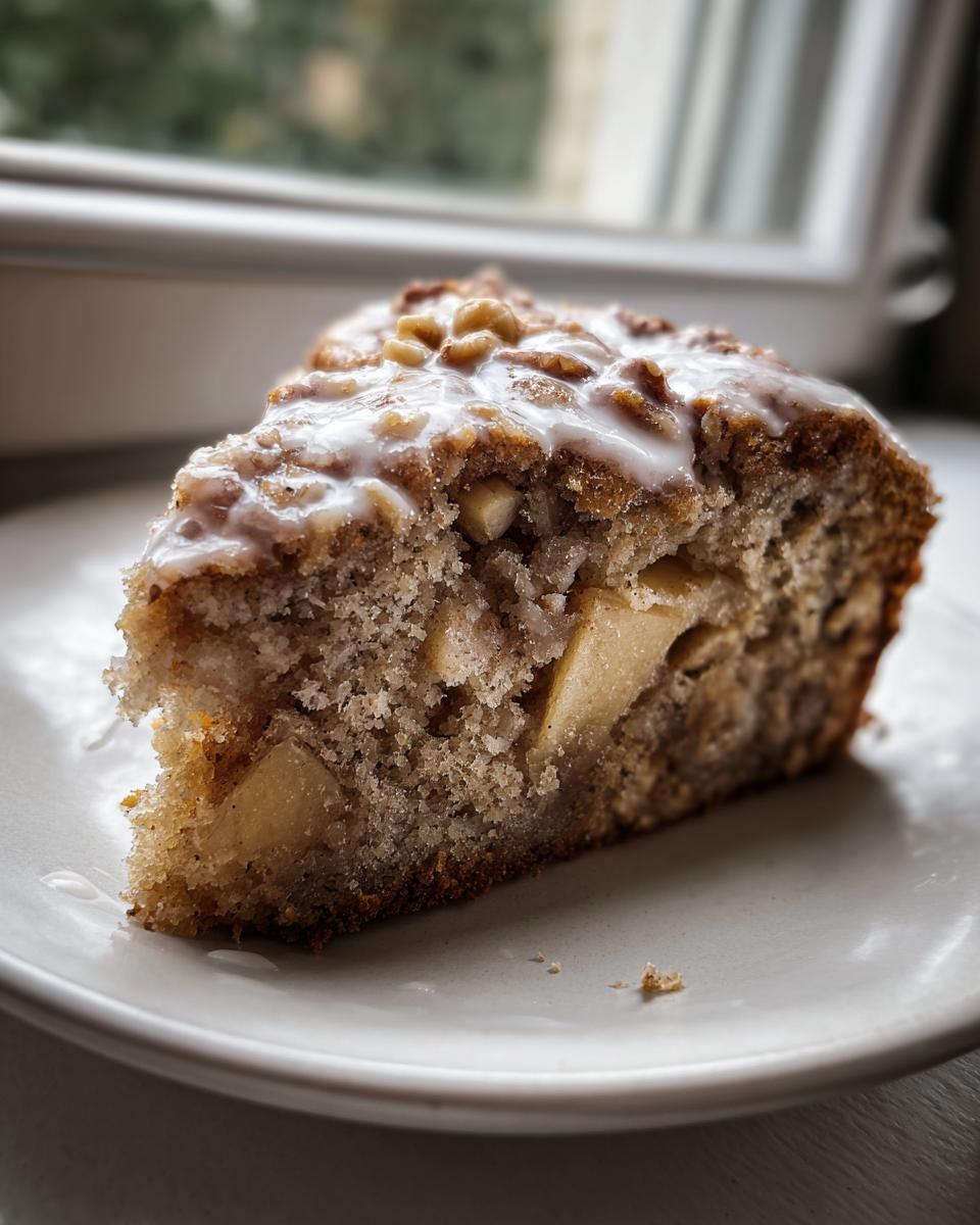 A close-up slice of moist jewish apple cake featuring visible apple chunks and a sweet walnut glaze.