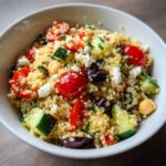 Close-up of a vibrant quinoa salad mixed with cherry tomatoes, cucumber, feta, and olives.