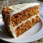 Close-up of a rich slice of carrot cake recipe showing shredded carrots and thick cream cheese frosting layers.