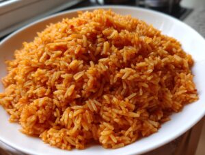 A close-up shot of perfectly cooked, bright orange jollof rice piled high on a white plate.