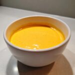 Close-up of a small white bowl filled with smooth, vibrant orange beer cheese dip.